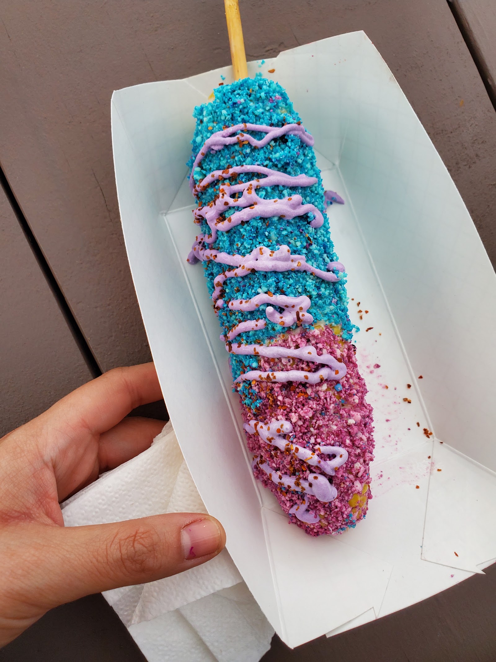 Elote on a stick coated in blue and pink unicorn topping